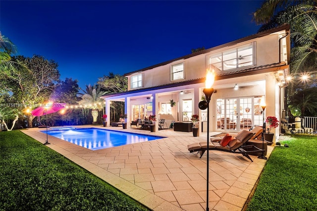 pool at night with french doors, a lawn, a fenced in pool, and a patio area