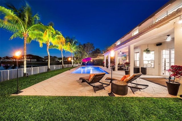 pool at twilight featuring ceiling fan, a patio area, a fenced in pool, fence, and a water view
