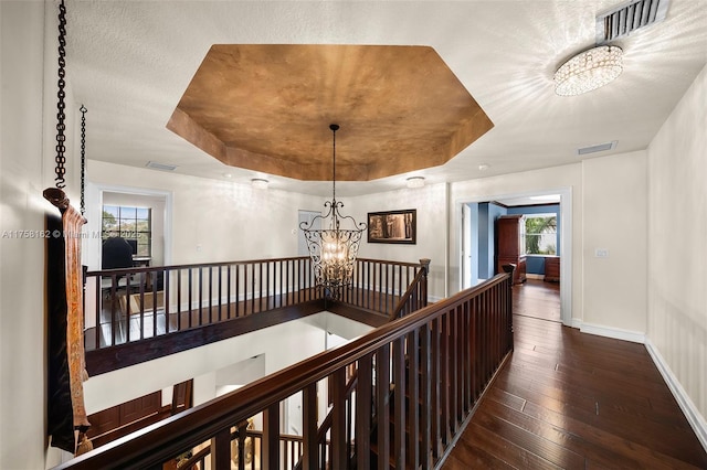 hall featuring visible vents, an upstairs landing, a raised ceiling, wood-type flooring, and a notable chandelier