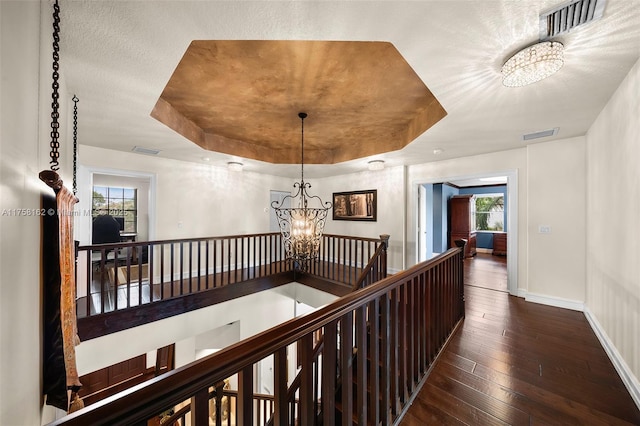 hallway with an upstairs landing, a notable chandelier, a tray ceiling, and hardwood / wood-style floors