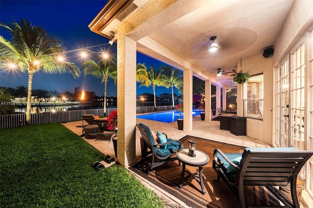 patio at night featuring a fenced backyard, a fenced in pool, a ceiling fan, and a yard