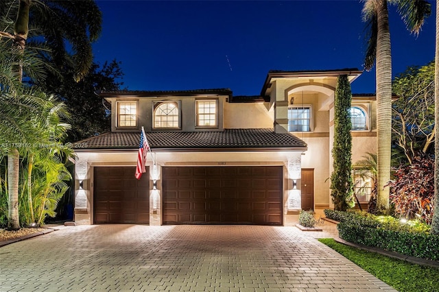 mediterranean / spanish-style home with a garage, stucco siding, a tile roof, and decorative driveway