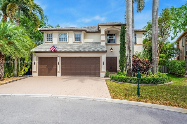 mediterranean / spanish home featuring driveway, a tile roof, a front yard, a garage, and stucco siding