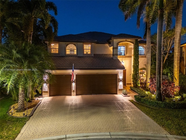 mediterranean / spanish home featuring stucco siding, decorative driveway, an attached garage, and a tiled roof