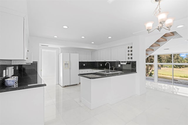 kitchen featuring a peninsula, white cabinets, white fridge with ice dispenser, dark countertops, and tasteful backsplash