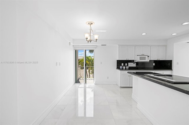 kitchen featuring dark countertops, an inviting chandelier, decorative backsplash, baseboards, and white microwave