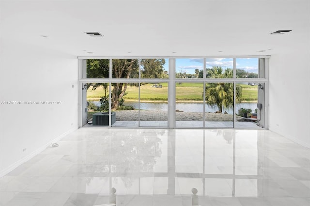 empty room with a wall of windows, visible vents, a water view, and baseboards