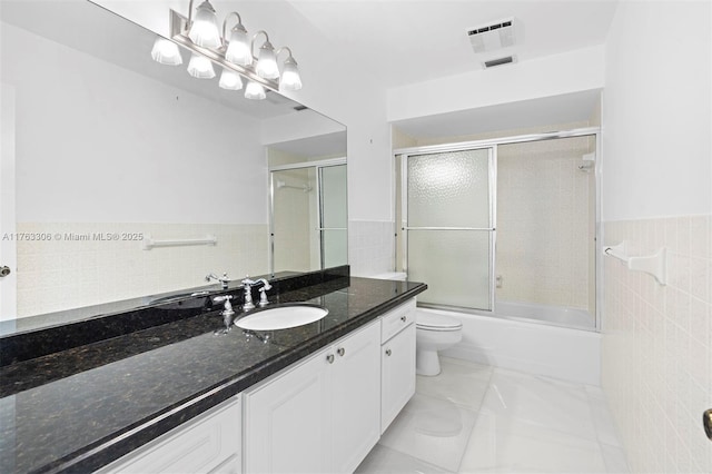 bathroom featuring visible vents, toilet, vanity, wainscoting, and tile walls