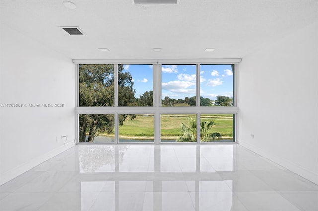 unfurnished room featuring visible vents, a wall of windows, and baseboards