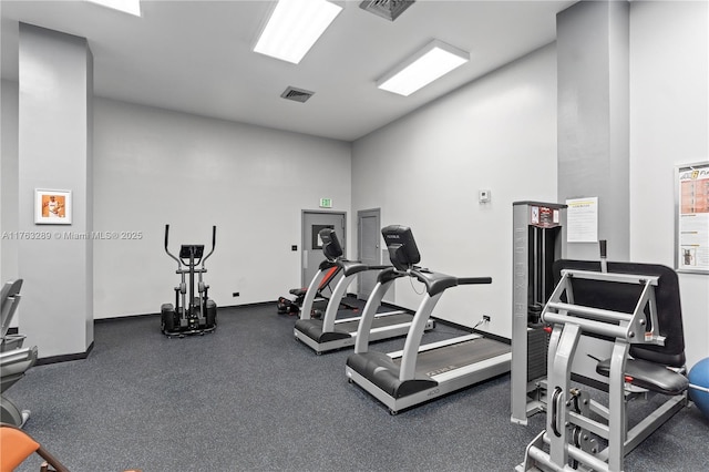 exercise room with visible vents, baseboards, and a towering ceiling