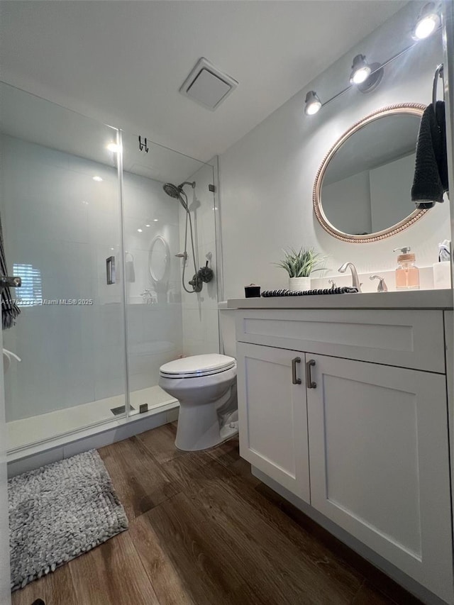 bathroom featuring visible vents, a shower stall, toilet, wood finished floors, and vanity