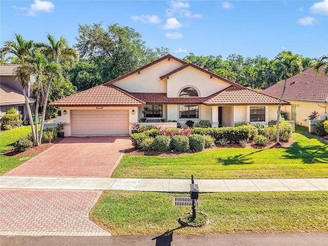 mediterranean / spanish-style home featuring an attached garage, stucco siding, a front lawn, a tiled roof, and decorative driveway