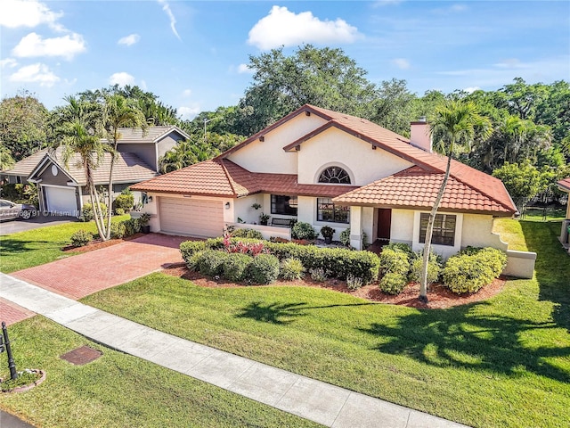 mediterranean / spanish-style house featuring a front yard, stucco siding, a chimney, a garage, and driveway