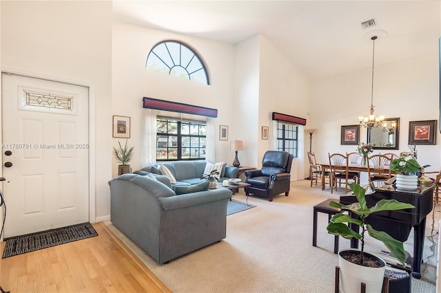 living room featuring light wood finished floors, a notable chandelier, visible vents, and a towering ceiling