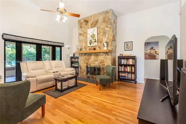 living room with arched walkways, a high ceiling, a fireplace, light wood finished floors, and ceiling fan