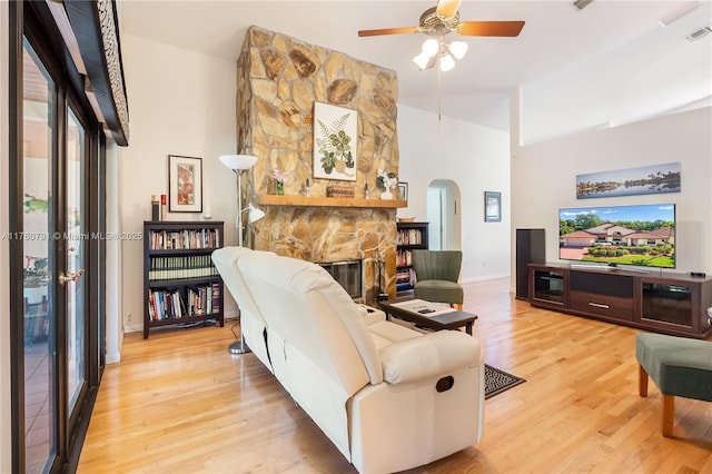 living room featuring light wood finished floors, visible vents, a fireplace, arched walkways, and a ceiling fan