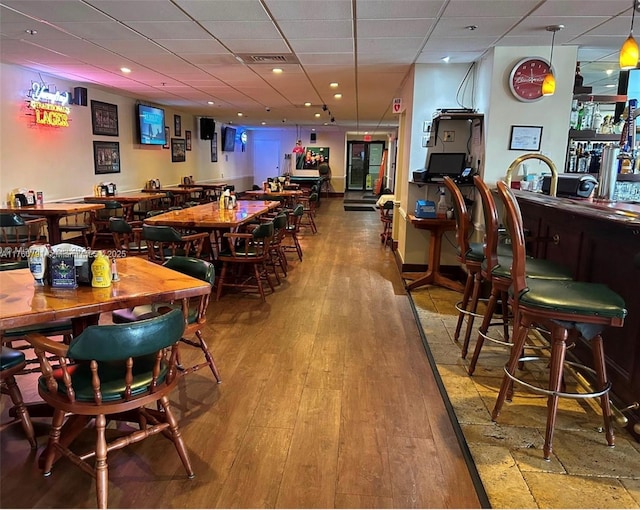 dining space with a community bar, visible vents, a paneled ceiling, and wood finished floors