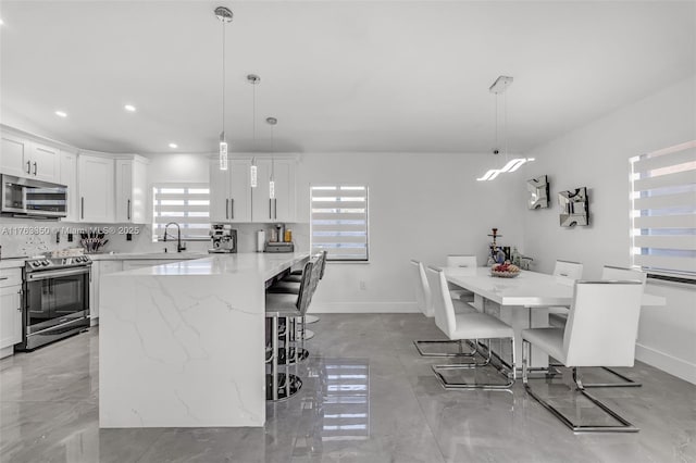 kitchen featuring white cabinetry, a sink, a breakfast bar, stainless steel appliances, and backsplash