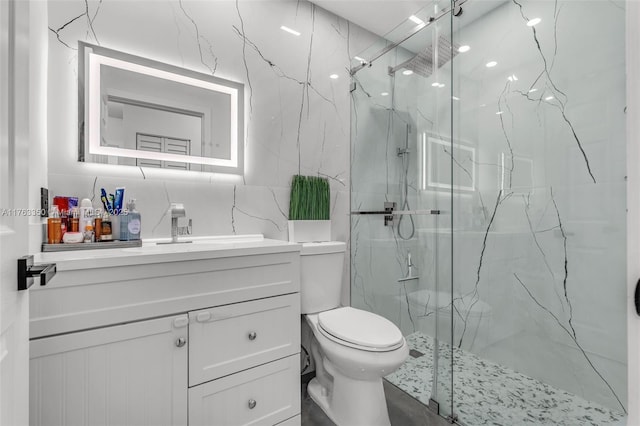 bathroom featuring toilet, a marble finish shower, tile walls, and vanity