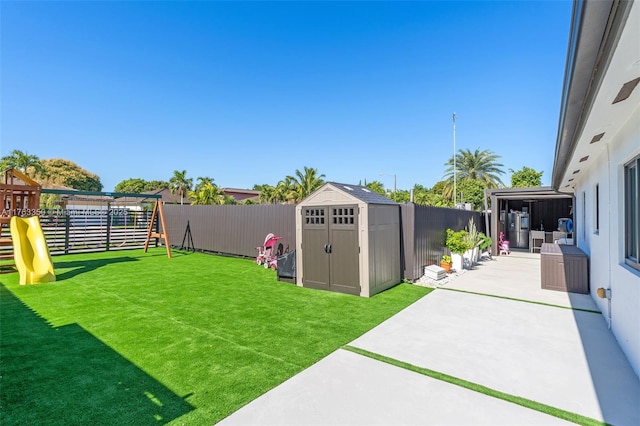 view of yard featuring a fenced backyard, a storage unit, an outbuilding, a patio, and a playground