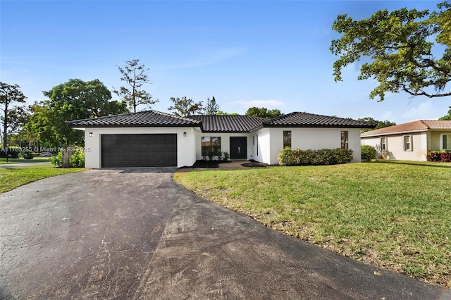 view of front facade featuring a tile roof, a front yard, stucco siding, a garage, and driveway