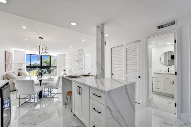 kitchen featuring open floor plan, white cabinetry, visible vents, decorative light fixtures, and light stone counters