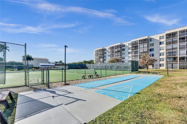 view of property's community with a gate, shuffleboard, a lawn, and fence