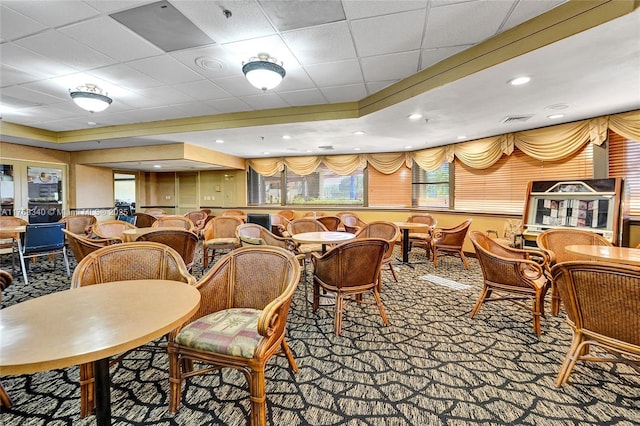 carpeted dining space with a drop ceiling, visible vents, and a raised ceiling