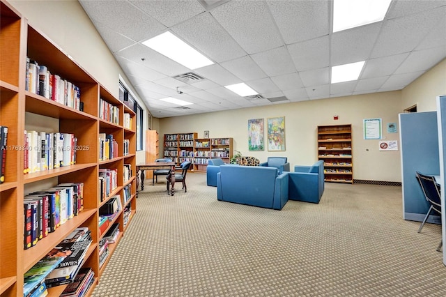interior space with a paneled ceiling, wall of books, visible vents, and carpet floors