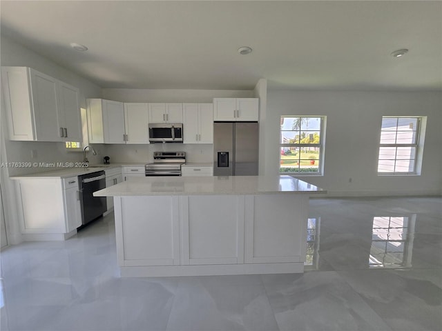 kitchen featuring a kitchen island, appliances with stainless steel finishes, white cabinets, and light countertops