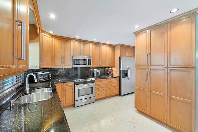 kitchen featuring dark stone countertops, light tile patterned floors, a sink, stainless steel appliances, and backsplash