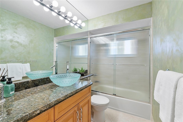 bathroom with tile patterned floors, toilet, vanity, and shower / bath combination with glass door