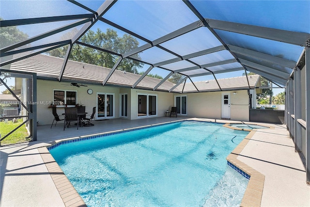 view of pool featuring a ceiling fan, glass enclosure, a patio area, and a pool with connected hot tub