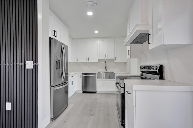 kitchen with light countertops, light wood-style flooring, stainless steel appliances, white cabinetry, and a sink