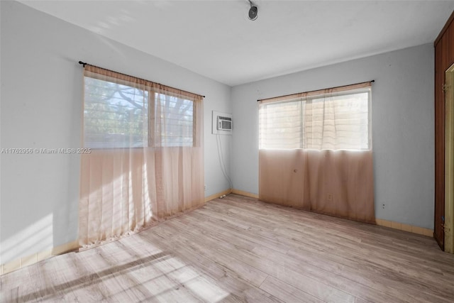 empty room featuring an AC wall unit, plenty of natural light, wood finished floors, and baseboards