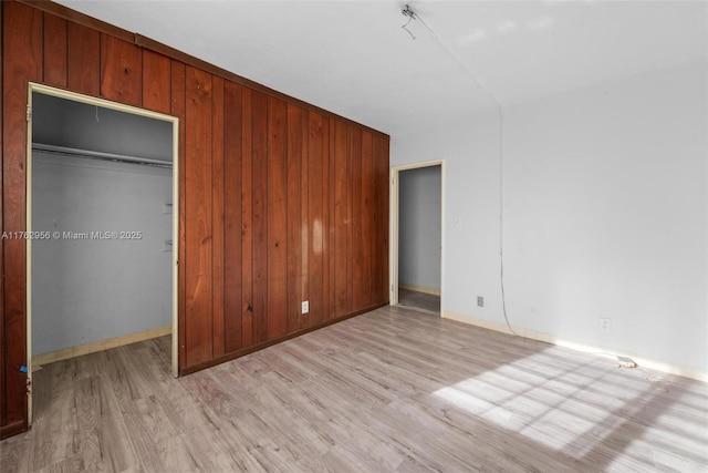 unfurnished bedroom featuring a closet, baseboards, wood walls, and light wood finished floors