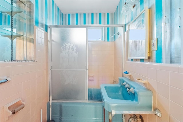 full bath featuring tile walls, bath / shower combo with glass door, and a sink