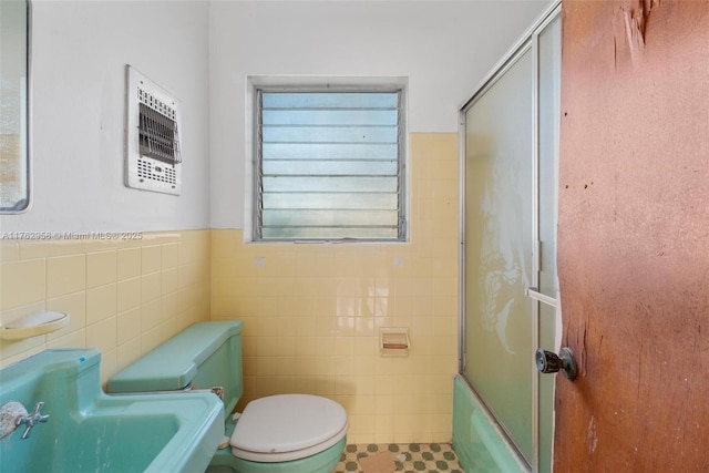 full bathroom with a wainscoted wall, enclosed tub / shower combo, toilet, and tile walls