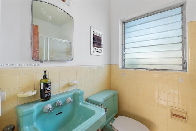 bathroom with a wainscoted wall, toilet, tile walls, and a sink