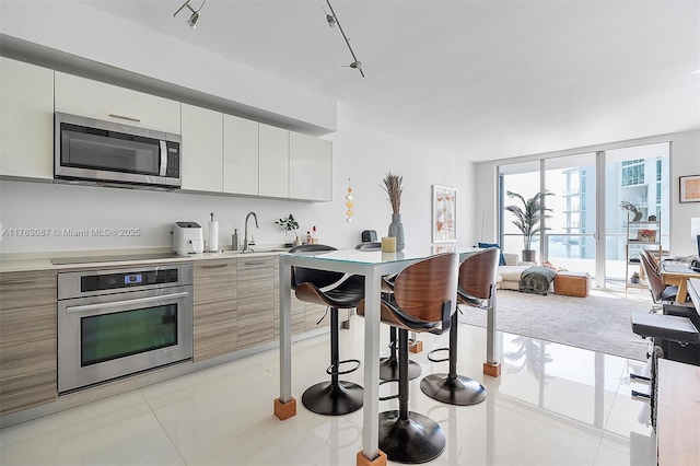 kitchen featuring modern cabinets, stainless steel appliances, light countertops, a wall of windows, and light tile patterned floors