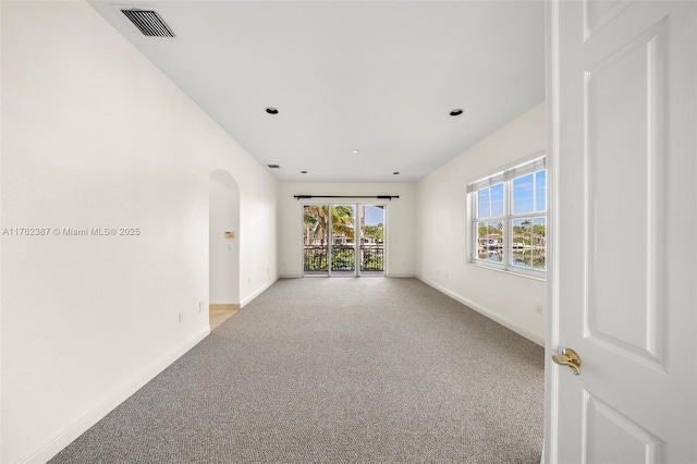 empty room featuring baseboards, light carpet, arched walkways, and visible vents