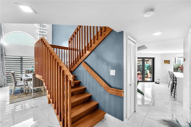 staircase featuring marble finish floor and a chandelier