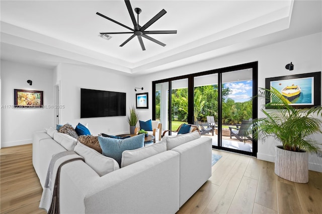 living area featuring a tray ceiling, light wood-style flooring, baseboards, and visible vents