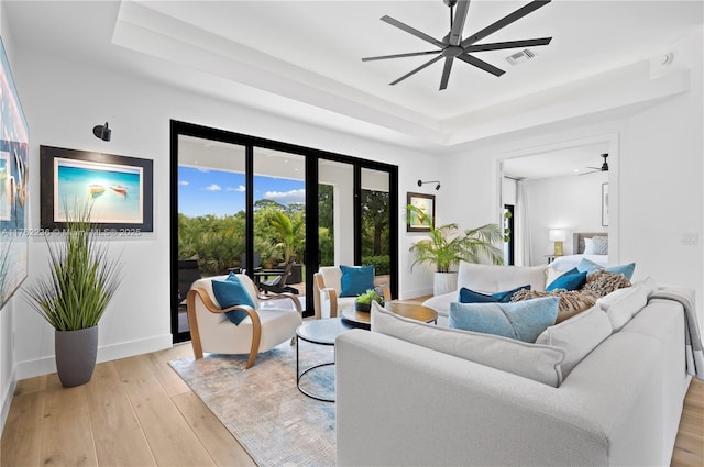 living room with light wood finished floors, visible vents, a raised ceiling, and ceiling fan