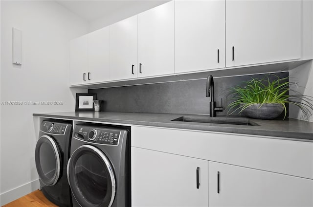 washroom with baseboards, washing machine and dryer, light wood-style floors, cabinet space, and a sink