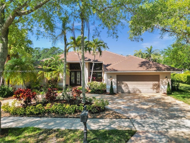 view of front of property featuring an attached garage, a tile roof, stucco siding, french doors, and driveway