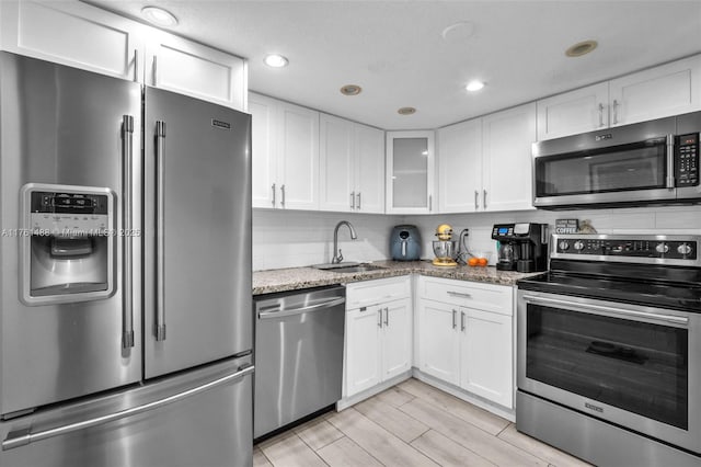 kitchen with a sink, light stone counters, stainless steel appliances, white cabinets, and decorative backsplash