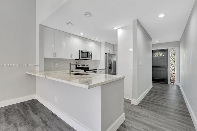 kitchen with dark wood-style floors, backsplash, a peninsula, and stainless steel appliances