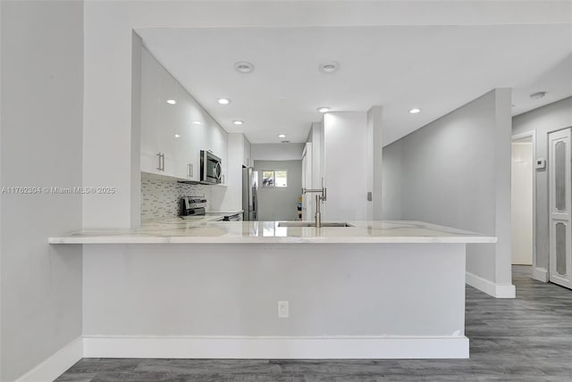 kitchen featuring a sink, backsplash, appliances with stainless steel finishes, white cabinets, and a peninsula