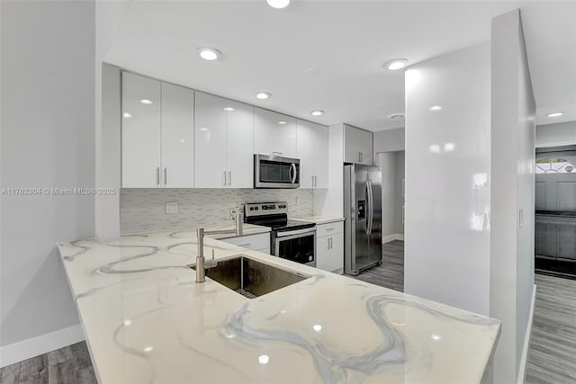 kitchen featuring light stone counters, wood finished floors, appliances with stainless steel finishes, modern cabinets, and tasteful backsplash